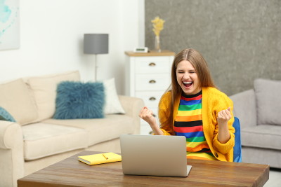 happy woman sat at laptop with yellow cardigan on